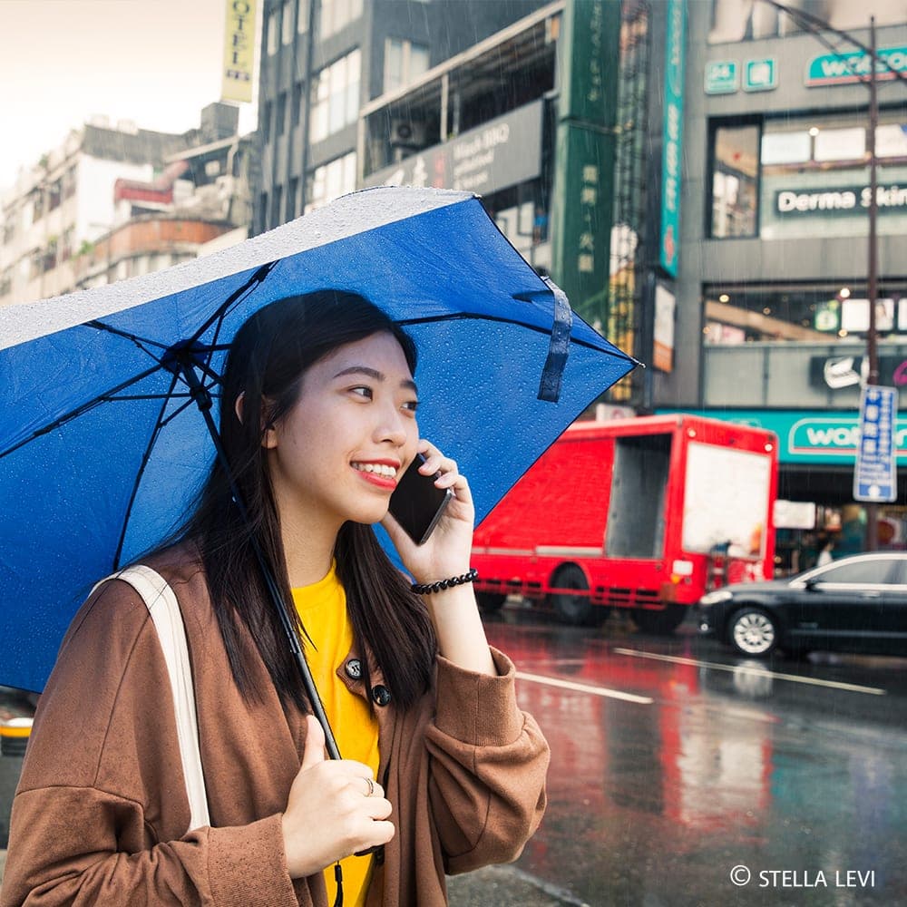 Photo of a smiling woman with a blue umbrella on a rainy street in Taipei