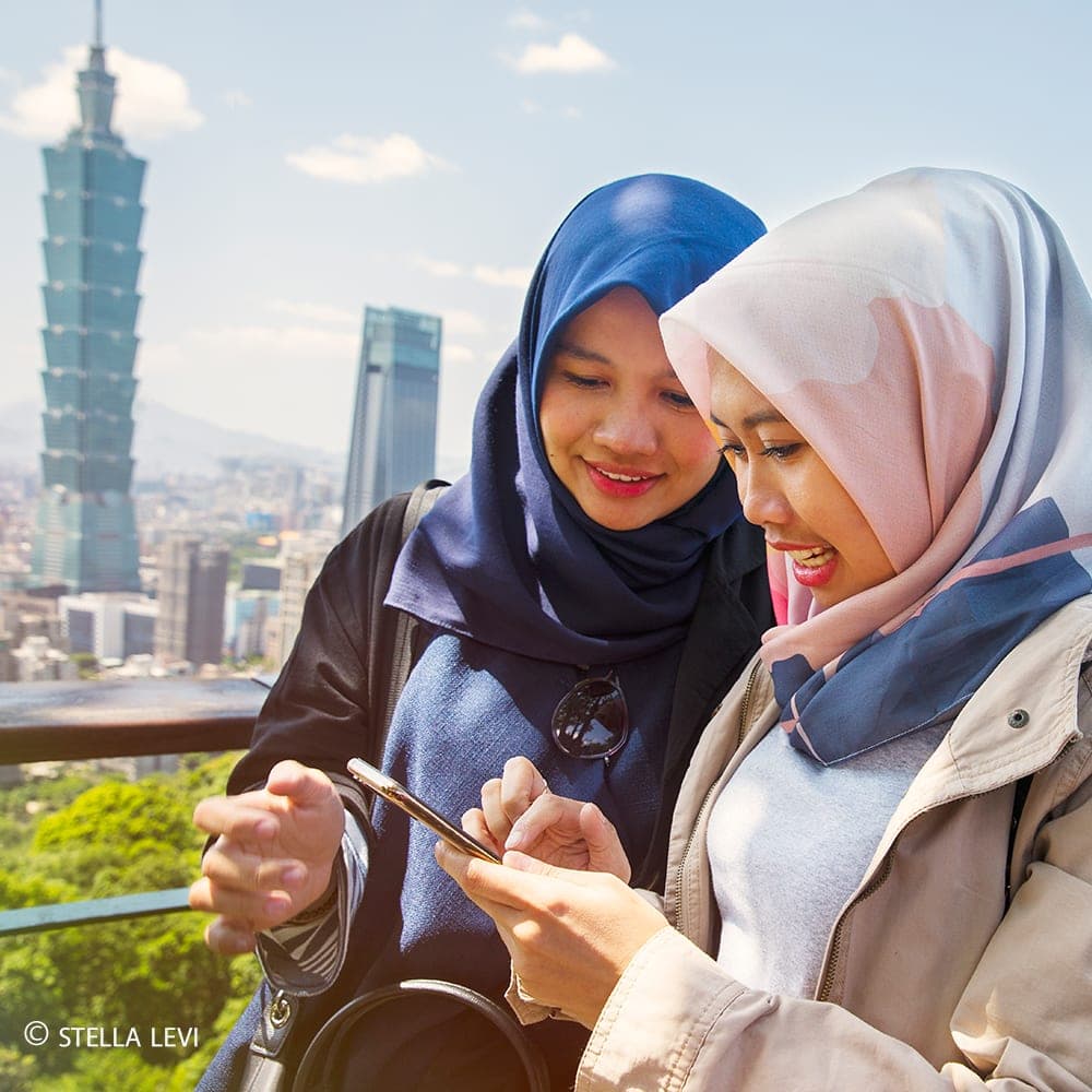 Photo of two women looking at a phone with Taipei 101 behind them