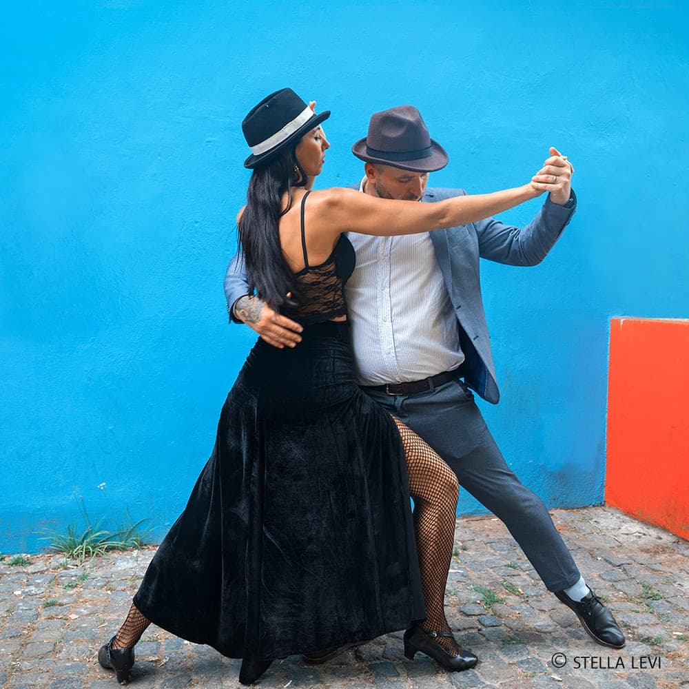 Photo of a couple dancing tango against a blue wall in Buenos Aires